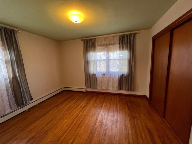 unfurnished bedroom featuring baseboard heating, a closet, and hardwood / wood-style floors