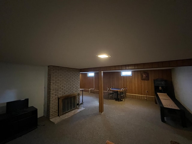 below grade area featuring a brick fireplace, carpet flooring, and wood walls