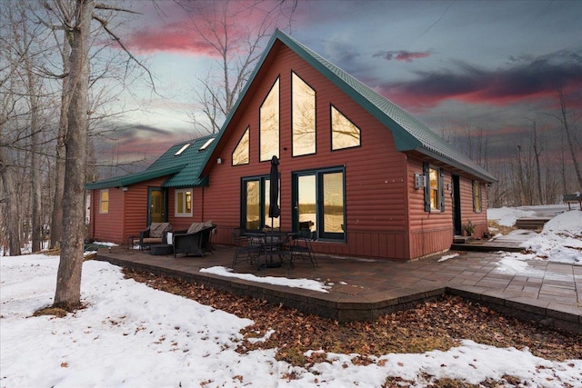 snow covered property featuring faux log siding and a patio