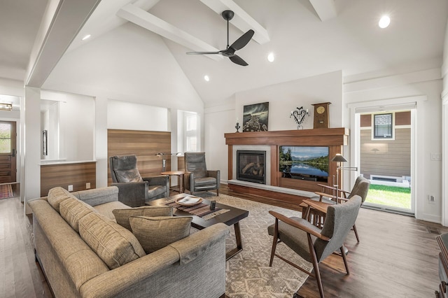 living area featuring beam ceiling, a ceiling fan, a glass covered fireplace, wood finished floors, and high vaulted ceiling