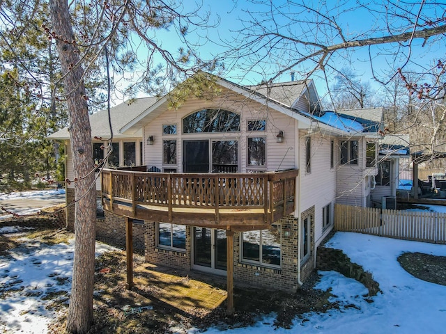 snow covered rear of property featuring fence, a deck, and brick siding