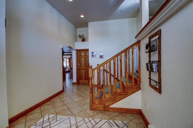 staircase with arched walkways, a high ceiling, tile patterned flooring, and baseboards