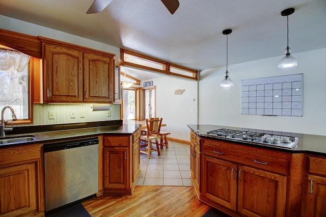 kitchen featuring appliances with stainless steel finishes, dark countertops, a sink, and brown cabinets