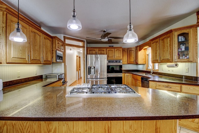 kitchen with a peninsula, appliances with stainless steel finishes, brown cabinetry, and glass insert cabinets