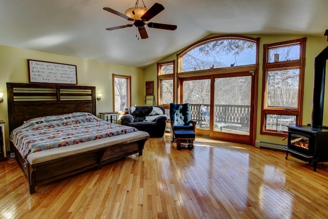 bedroom with a wood stove, access to outside, light wood-style flooring, and a baseboard radiator