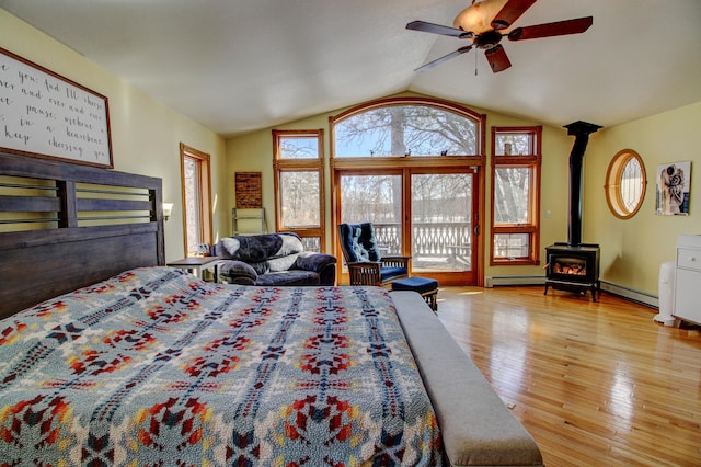 bedroom featuring a baseboard radiator, wood finished floors, a wood stove, access to outside, and vaulted ceiling