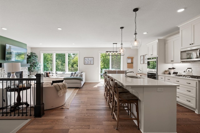 kitchen with dark wood-style floors, appliances with stainless steel finishes, a sink, white cabinetry, and backsplash