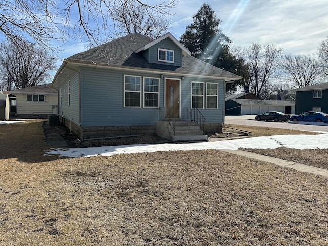 bungalow-style house featuring central AC unit and a shingled roof