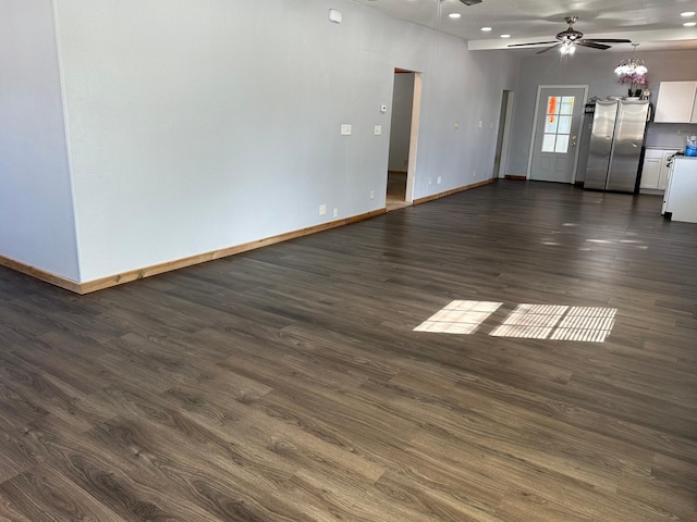 empty room with ceiling fan with notable chandelier, dark wood-style floors, and baseboards