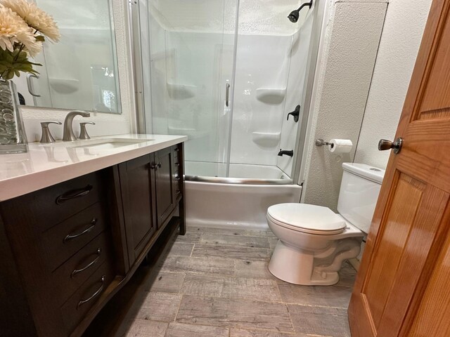 full bathroom featuring vanity, wood finished floors, enclosed tub / shower combo, toilet, and a textured wall