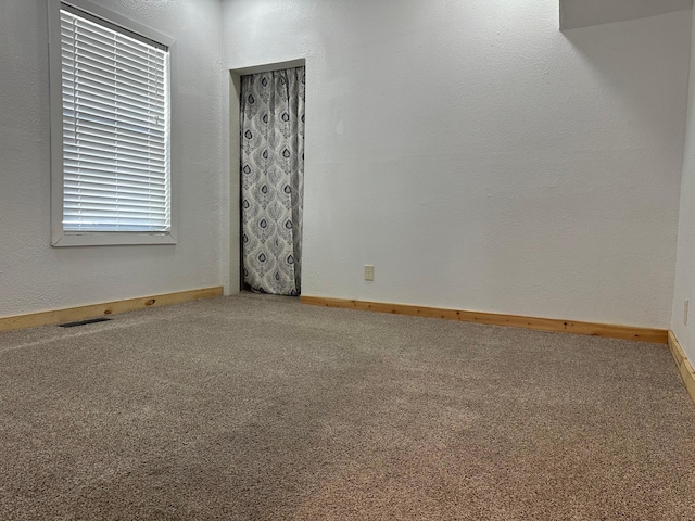 spare room featuring visible vents, baseboards, carpet flooring, and a textured wall