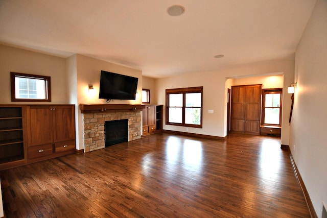 unfurnished living room featuring a stone fireplace, dark wood-style flooring, and baseboards