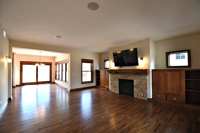 unfurnished living room with a stone fireplace, a notable chandelier, visible vents, baseboards, and dark wood-style floors