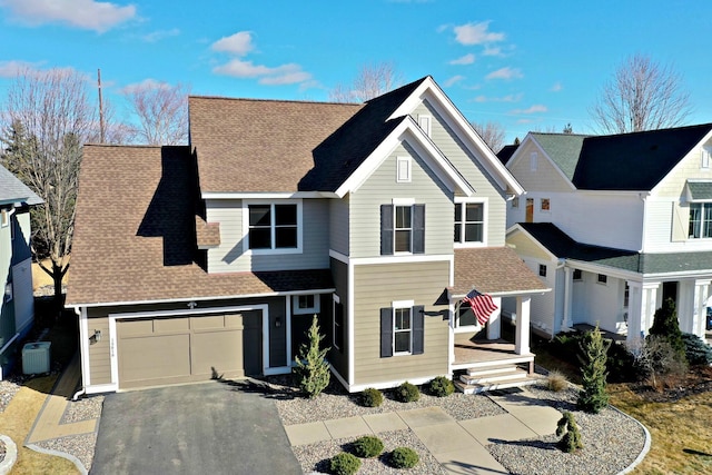 traditional home featuring a garage, central air condition unit, aphalt driveway, and roof with shingles