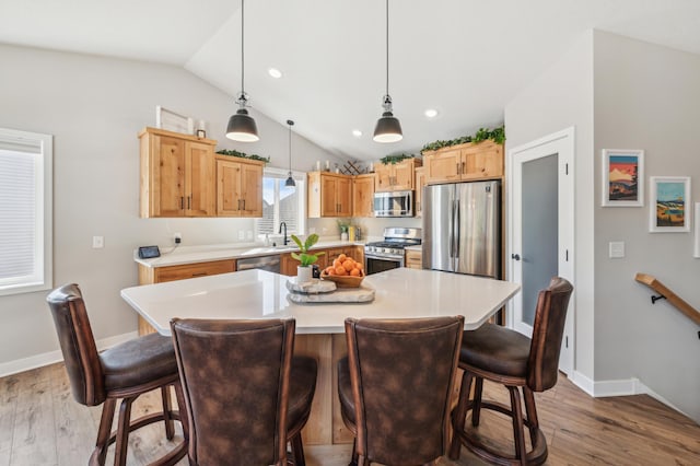 kitchen featuring stainless steel appliances, light countertops, vaulted ceiling, and light wood finished floors