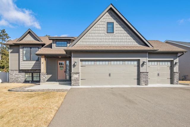 view of front of house with a garage, stone siding, aphalt driveway, and roof with shingles