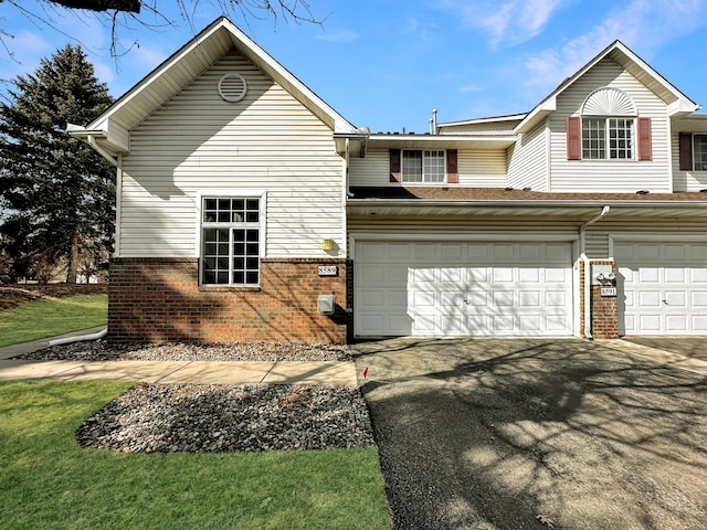 view of front of house featuring aphalt driveway, a front yard, brick siding, and a garage