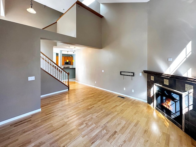 unfurnished living room with stairs, baseboards, wood finished floors, and a tile fireplace