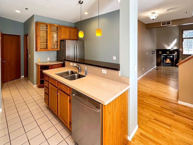 kitchen with a sink, hanging light fixtures, appliances with stainless steel finishes, brown cabinetry, and a glass covered fireplace