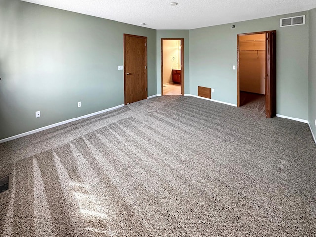 unfurnished bedroom with baseboards, visible vents, a walk in closet, a textured ceiling, and a closet