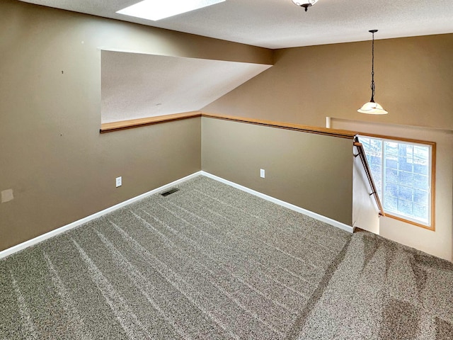 carpeted spare room featuring lofted ceiling, a textured ceiling, visible vents, and baseboards