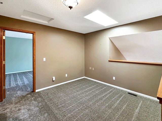 carpeted spare room with a textured ceiling, attic access, visible vents, and baseboards