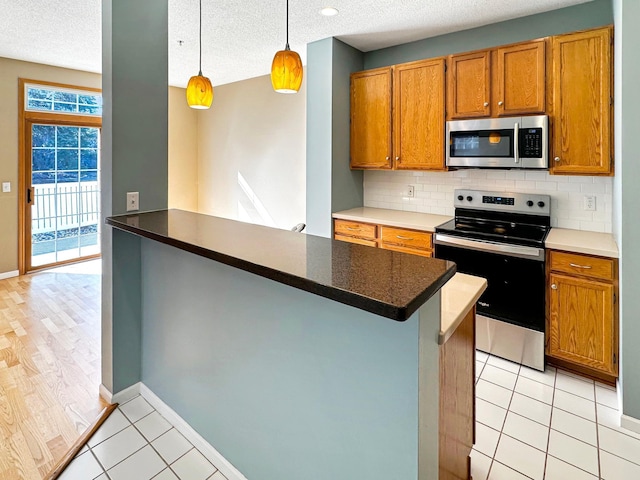 kitchen featuring light tile patterned floors, stainless steel appliances, brown cabinets, and decorative backsplash