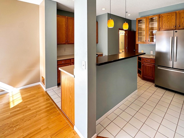 kitchen featuring brown cabinetry, glass insert cabinets, freestanding refrigerator, hanging light fixtures, and light tile patterned flooring