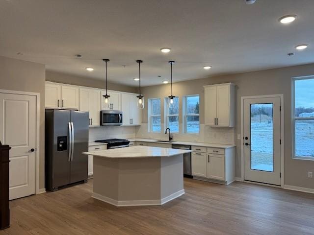 kitchen featuring a kitchen island, appliances with stainless steel finishes, wood finished floors, light countertops, and white cabinetry