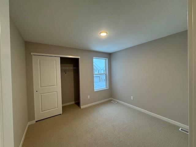 unfurnished bedroom with light carpet, baseboards, visible vents, and a closet