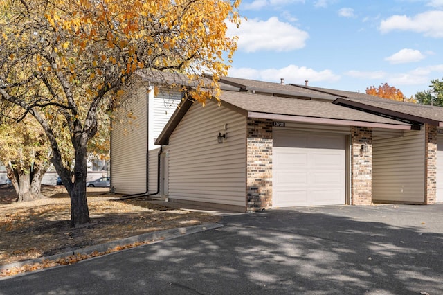 view of home's exterior featuring a garage, brick siding, roof with shingles, and aphalt driveway