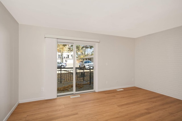 spare room with light wood-style floors, baseboards, visible vents, and brick wall