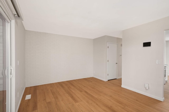 spare room featuring light wood finished floors, brick wall, visible vents, and baseboards