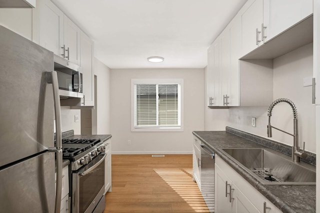 kitchen with white cabinets, dark countertops, light wood-style flooring, appliances with stainless steel finishes, and a sink