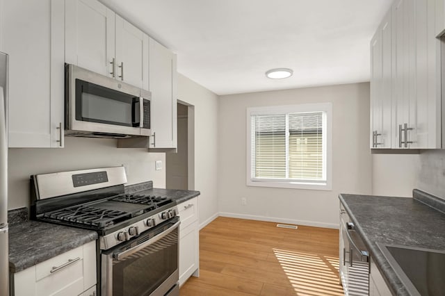 kitchen with baseboards, dark countertops, light wood-style flooring, stainless steel appliances, and white cabinetry