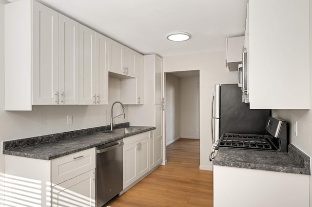 kitchen featuring stainless steel appliances, dark countertops, a sink, and white cabinetry