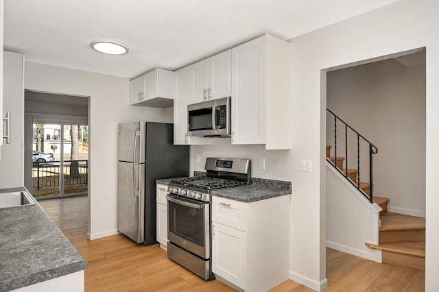 kitchen with stainless steel appliances, light wood-type flooring, white cabinetry, and dark countertops