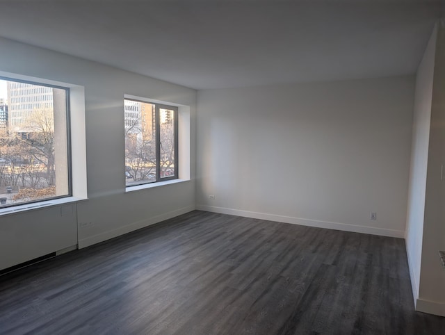 unfurnished room with plenty of natural light, baseboards, and dark wood-style flooring