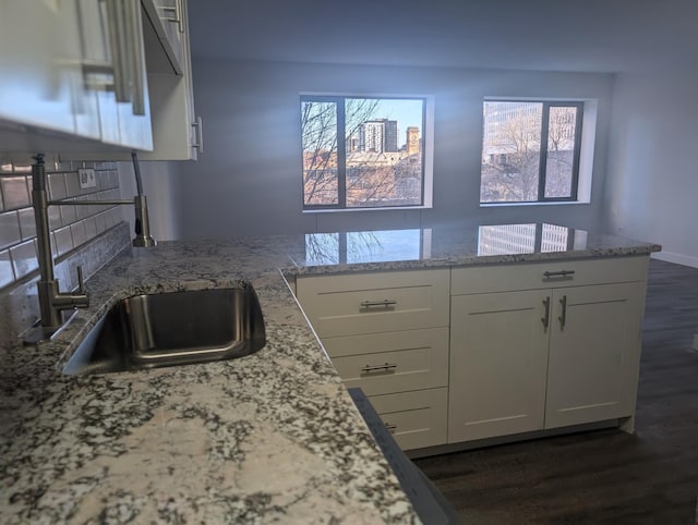 kitchen featuring light stone counters, dark wood-type flooring, a peninsula, white cabinetry, and a sink