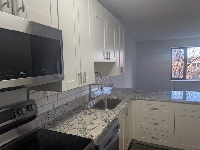 kitchen with stainless steel appliances, decorative backsplash, white cabinets, a sink, and light stone countertops