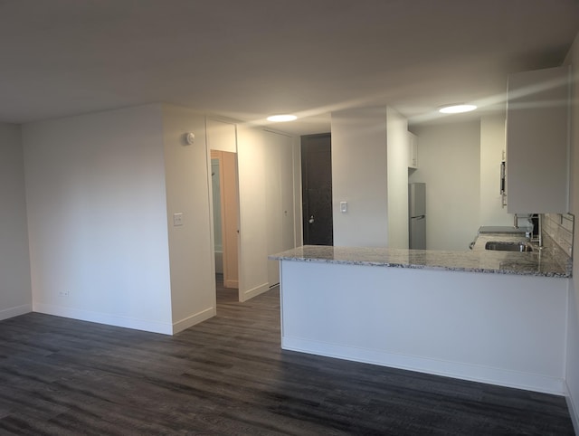 kitchen with light stone counters, freestanding refrigerator, dark wood-style flooring, and a sink