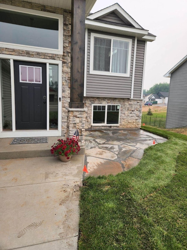 view of exterior entry with a yard, stone siding, and fence