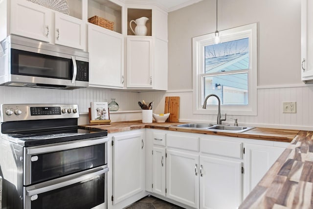 kitchen featuring wooden counters, wainscoting, white cabinets, stainless steel appliances, and a sink