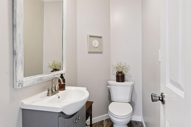 half bath featuring baseboards, toilet, wood finished floors, and vanity