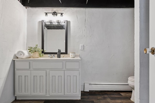 bathroom featuring baseboard heating, wood finished floors, vanity, and toilet