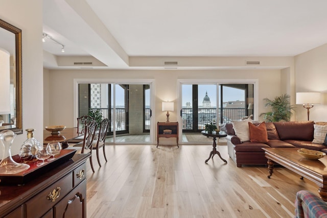 living room with a view of city, rail lighting, visible vents, and light wood-style floors