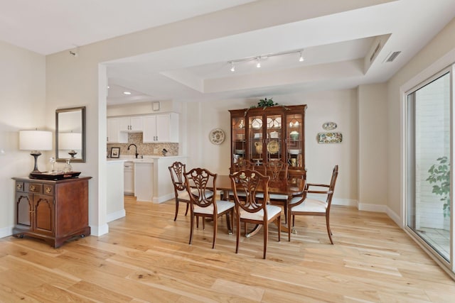 dining area featuring baseboards, a raised ceiling, visible vents, and light wood-style floors