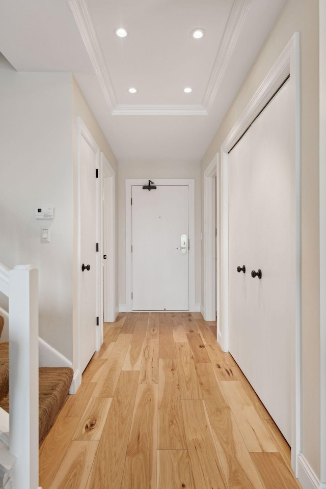 corridor featuring ornamental molding, a tray ceiling, light wood finished floors, and recessed lighting