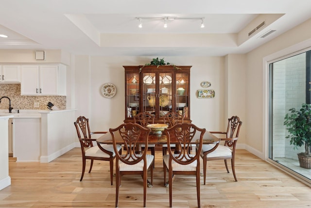 dining space featuring light wood finished floors, visible vents, a tray ceiling, and baseboards