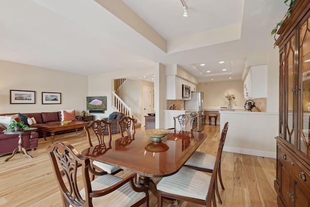 dining room with stairs, recessed lighting, a raised ceiling, and light wood-style floors